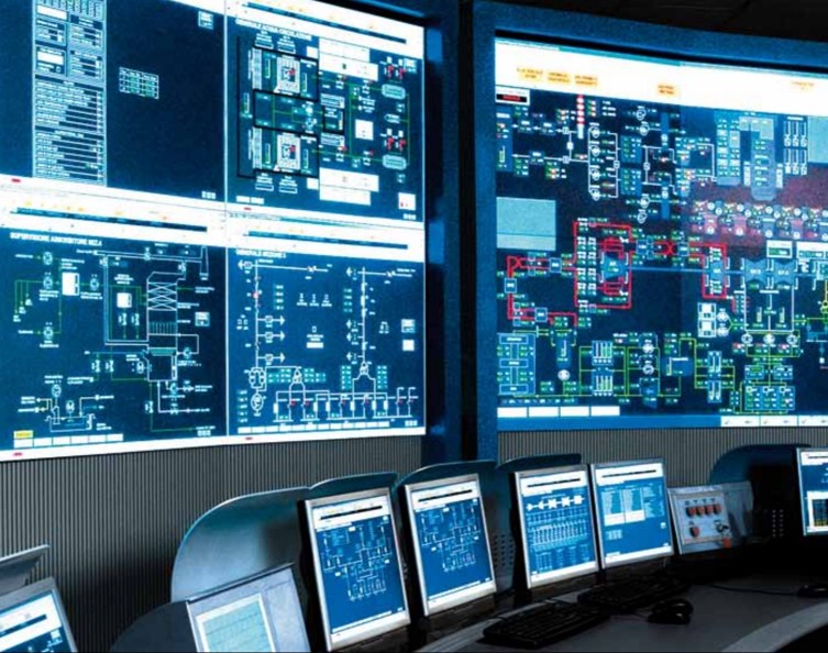 Industrial control room with wall-mounted SCADA monitors displaying process diagrams